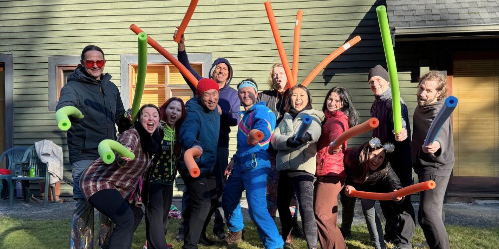 A laughing group holding colorful pool noodles outside the Joymaker Mansion